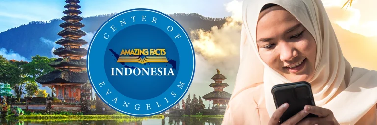 A smiling woman in a light-colored hijab looks at her smartphone. Beside her is a circular logo with the map of Indonesia and the text "Center of Evangelism – Amazing Facts Indonesia." In the background is a scenic view of a traditional Balinese temple with a tiered roof surrounded by water, lush greenery, and misty mountains under a warm, glowing sky