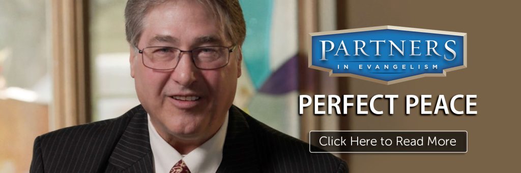 Man smiling and standing next to a sign that says "Partners In Evangelism"